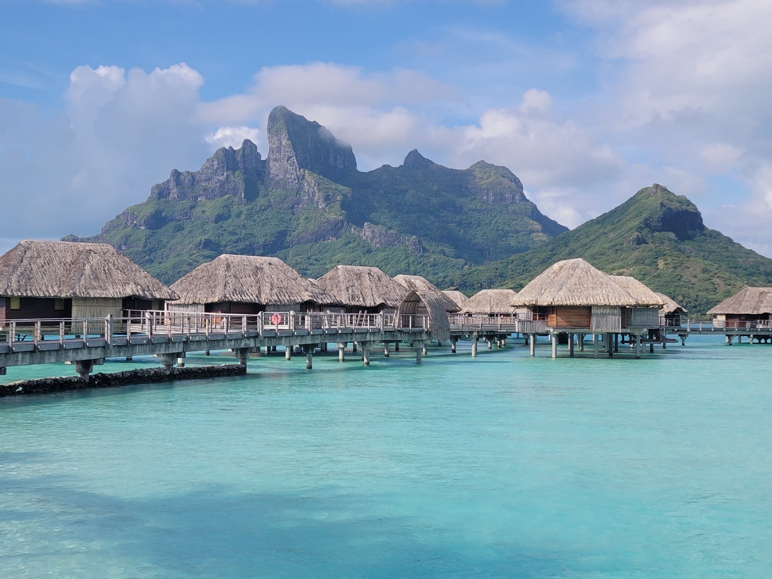Row of thatched overwater bungalows at Four Seasons Bora Bora with volcanic peaks behind