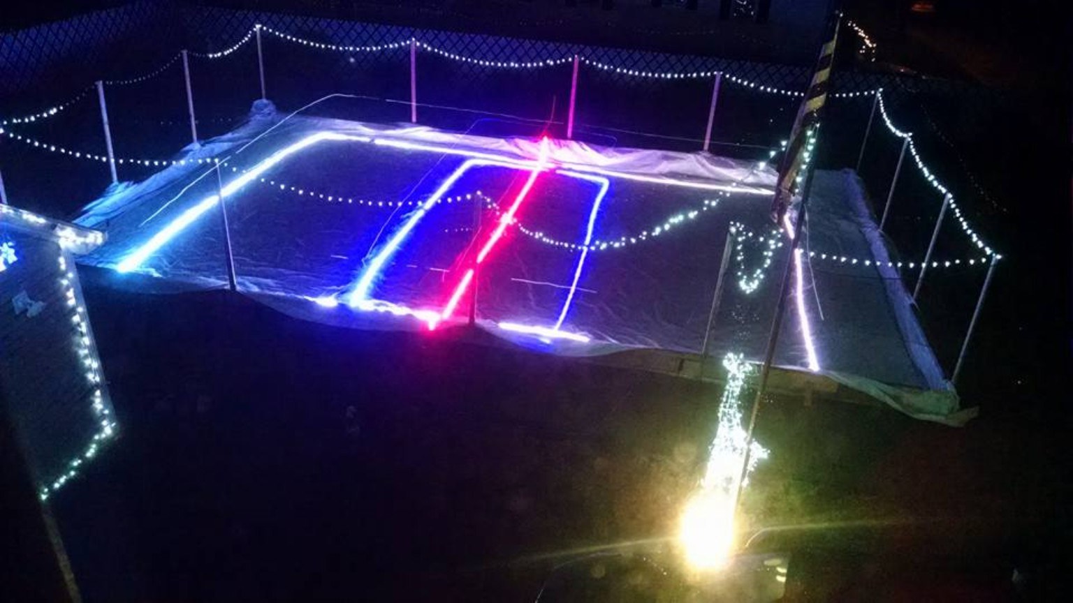 Backyard rink at night with colored LED lights glowing on the ice