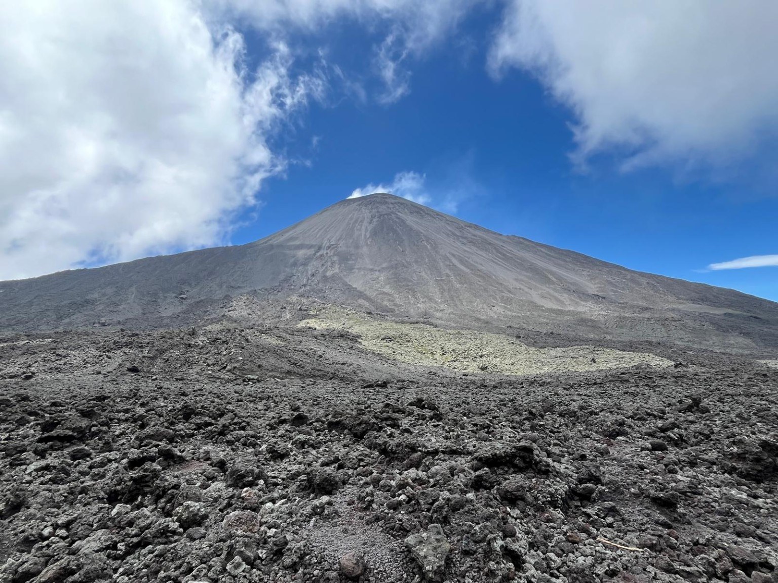 Bare cone of Volcán de Pacaya rising above a wide black lava field under blue sky