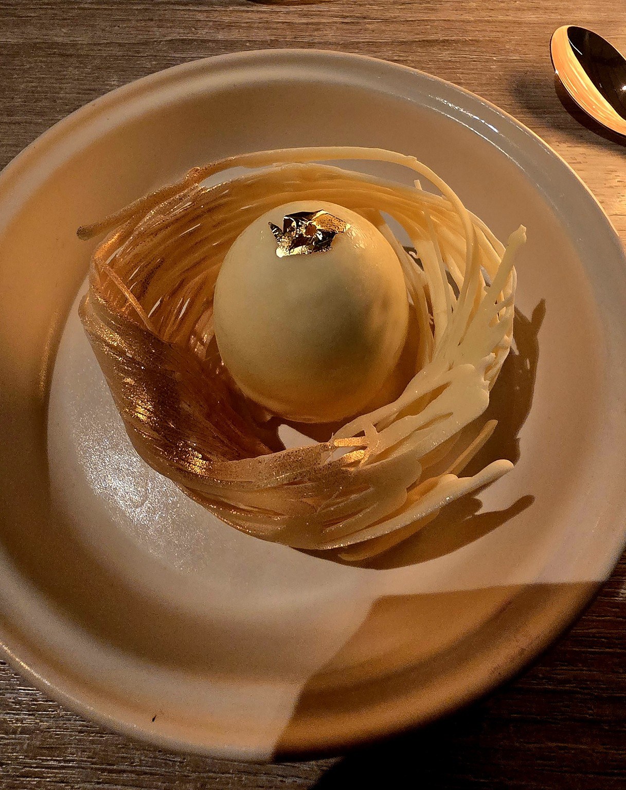Elegant Spanish dessert plated as a golden nest with a sphere on top