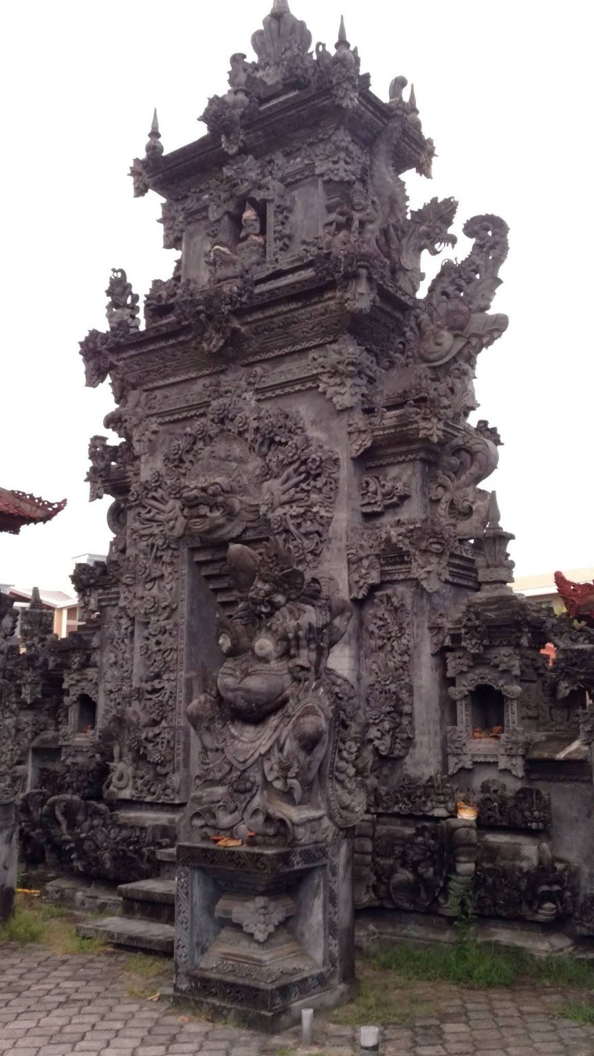 A detailed Balinese stone shrine carved with guardians, mythic figures, and floral patterns