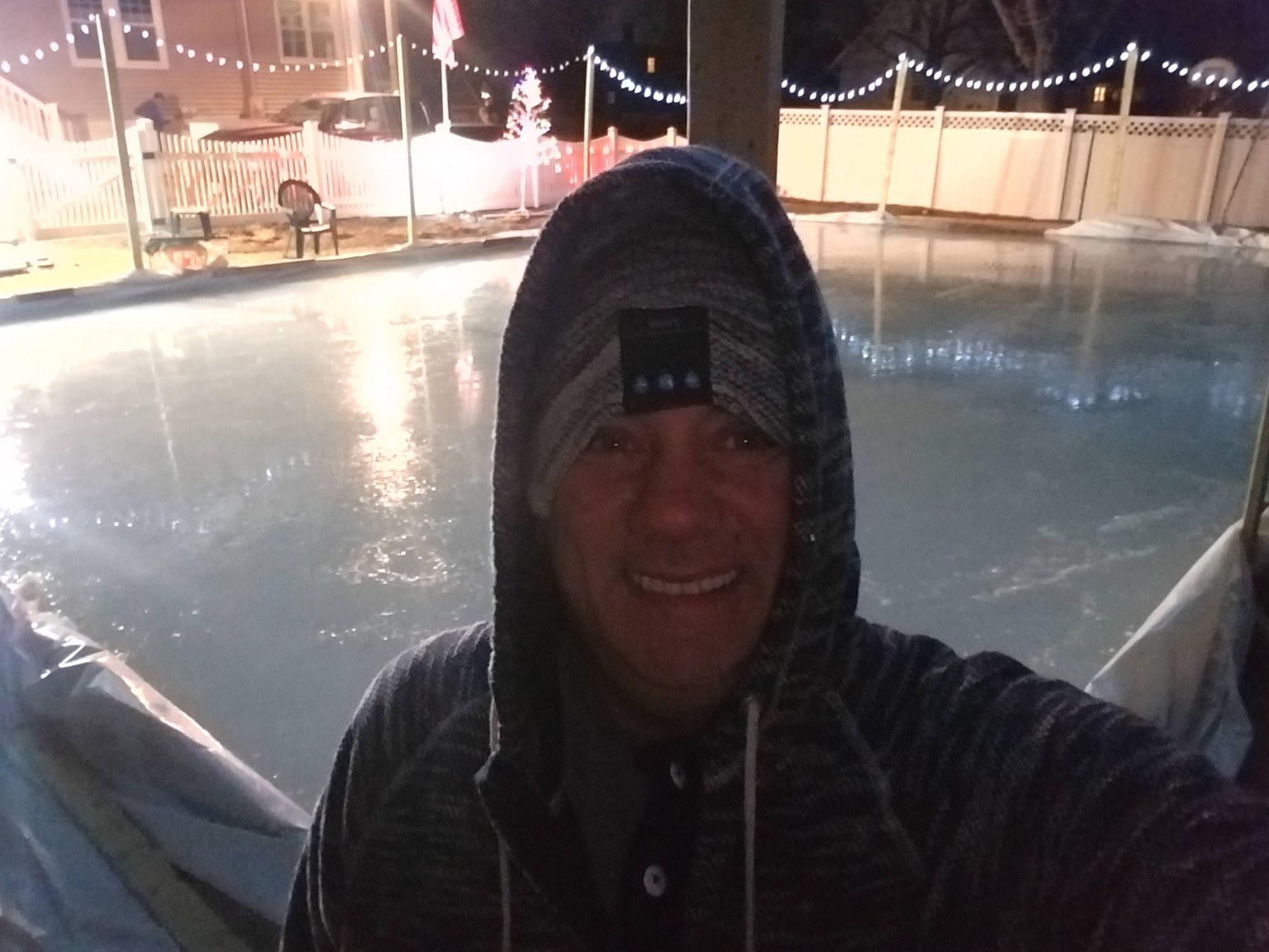 Rink keeper on backyard ice at night under colored lights