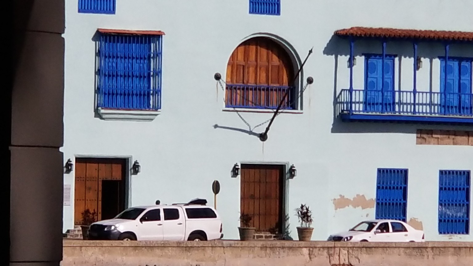 Whitewashed Cuban colonial facade with deep blue louvered shutters and an arched balcony
