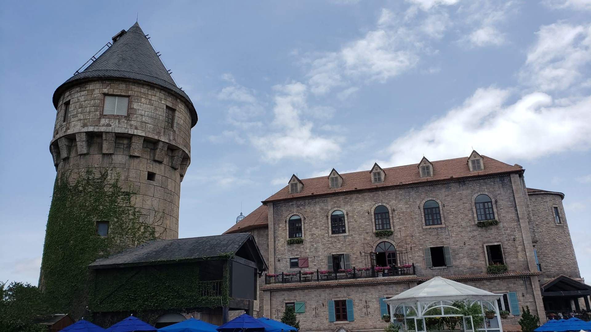Ivy-covered round tower and stone manor building at Ba Na Hills with blue umbrellas below