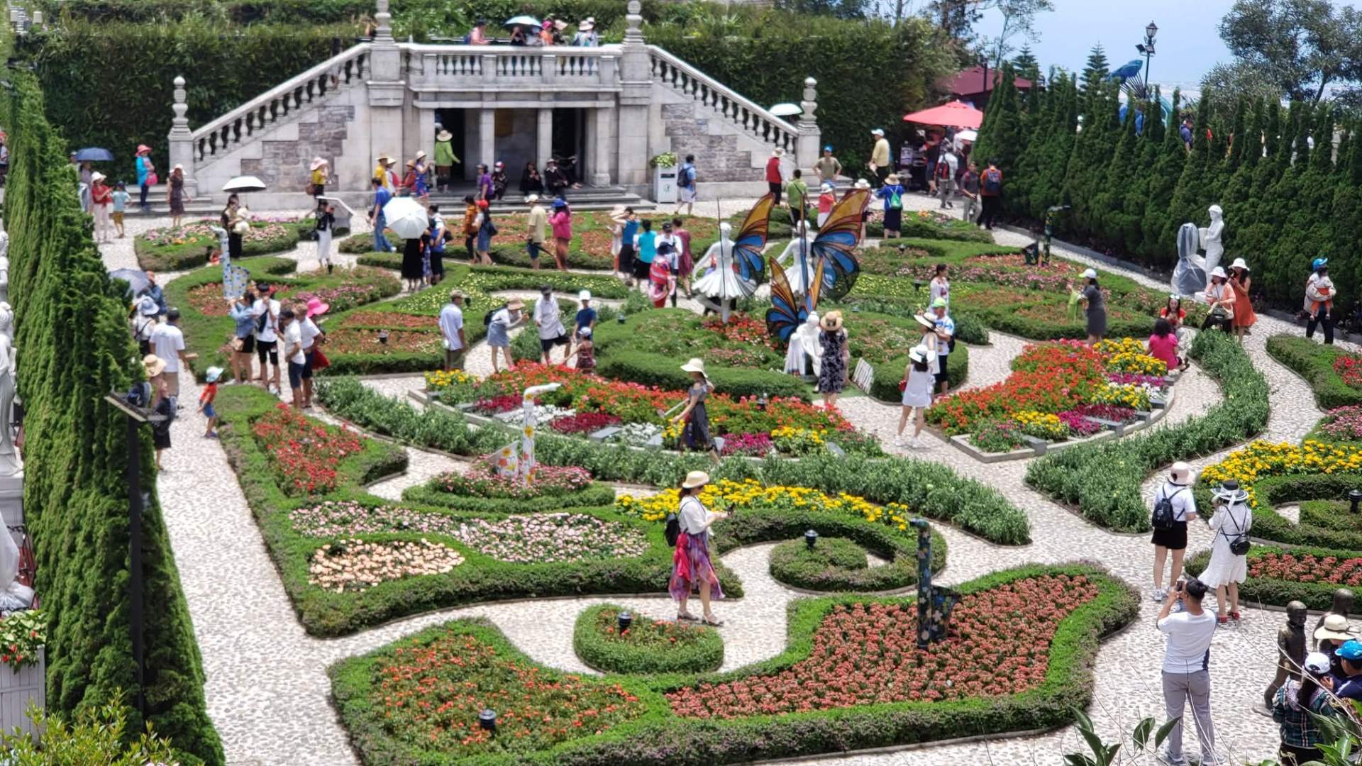 Formal French-style flower garden at Ba Na Hills with crowds and statues