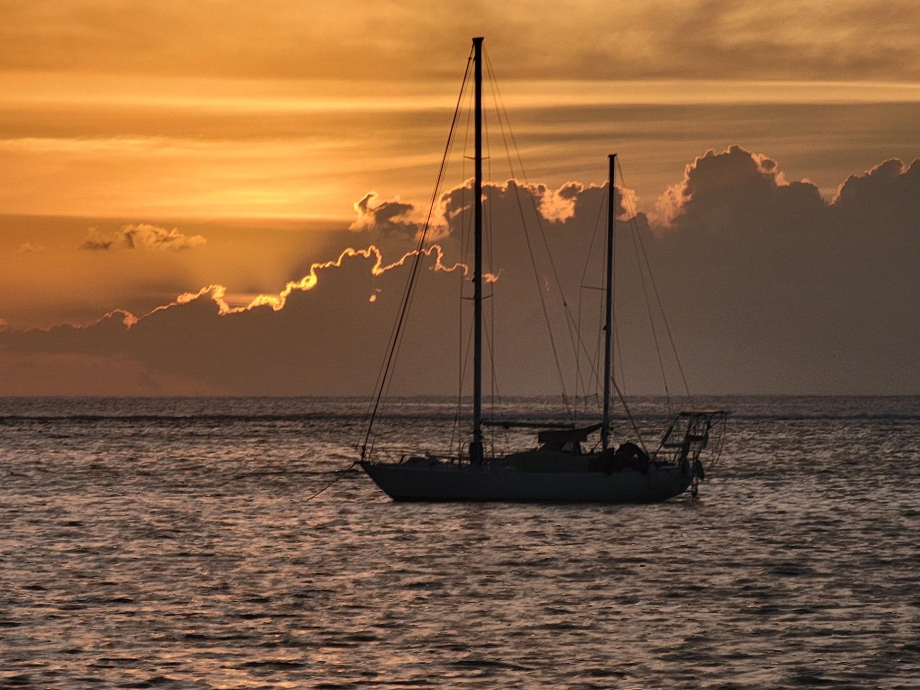 Sailboat silhouetted against an orange Tahiti sunset with backlit clouds