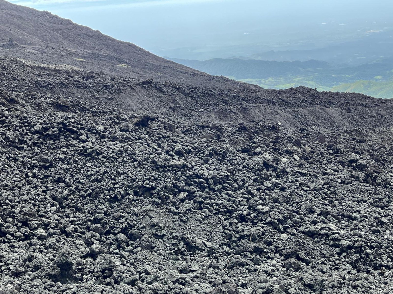 Field of dark, broken lava rock on the upper slopes of Pacaya, with hazy lowlands beyond