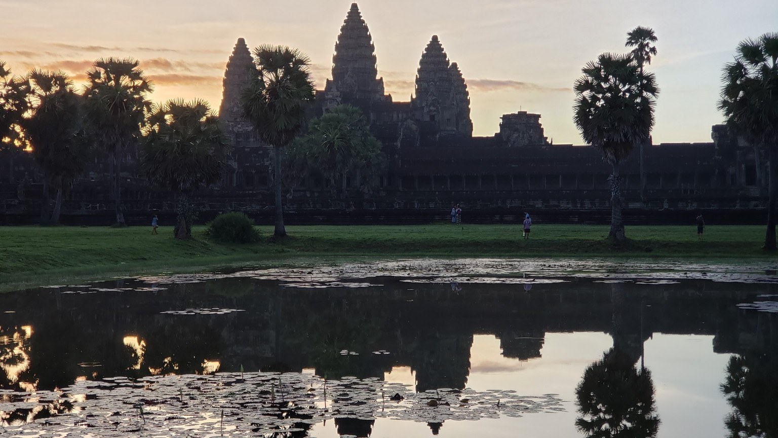 Angkor Wat at sunrise, its five lotus-bud towers reflected in a lily pond framed by palm trees