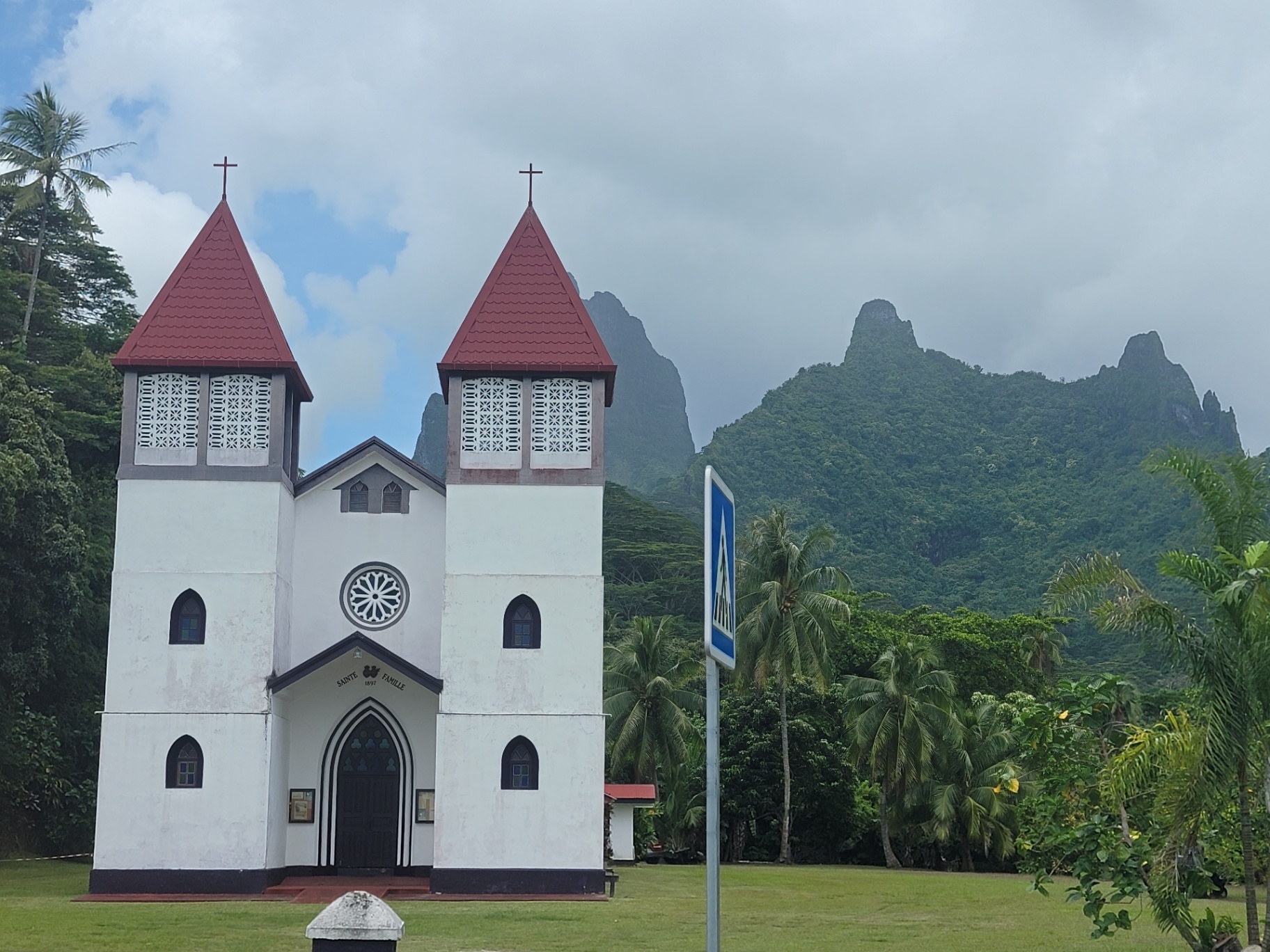 White Sainte Famille church in Haapiti, Moorea with twin red steeples and dramatic green peaks behind