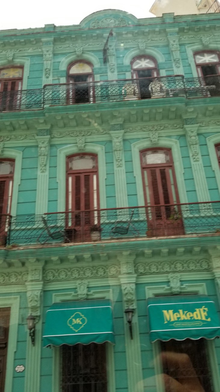 Turquoise three-story colonial building in Havana with red-shuttered windows and iron balconies