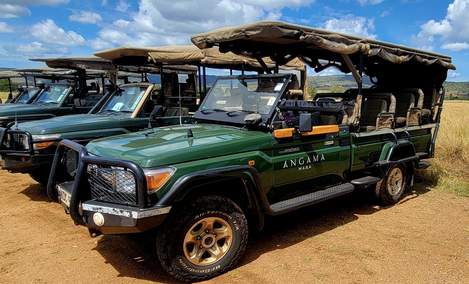 Open-sided Land Cruiser safari vehicles lined up at a dirt airstrip in the Mara