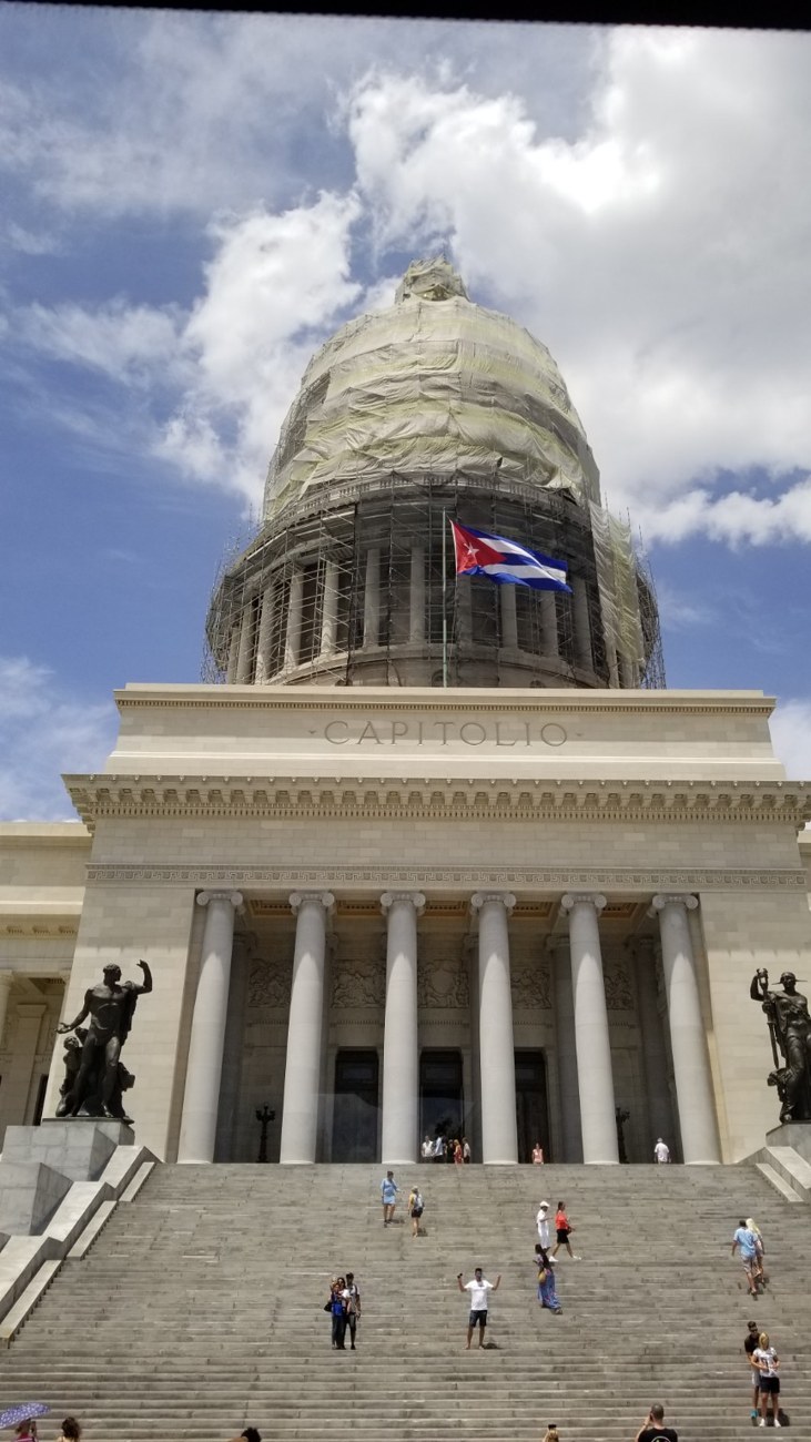 Cuban flag flying in front of the Capitolio, its dome wrapped in restoration scaffolding