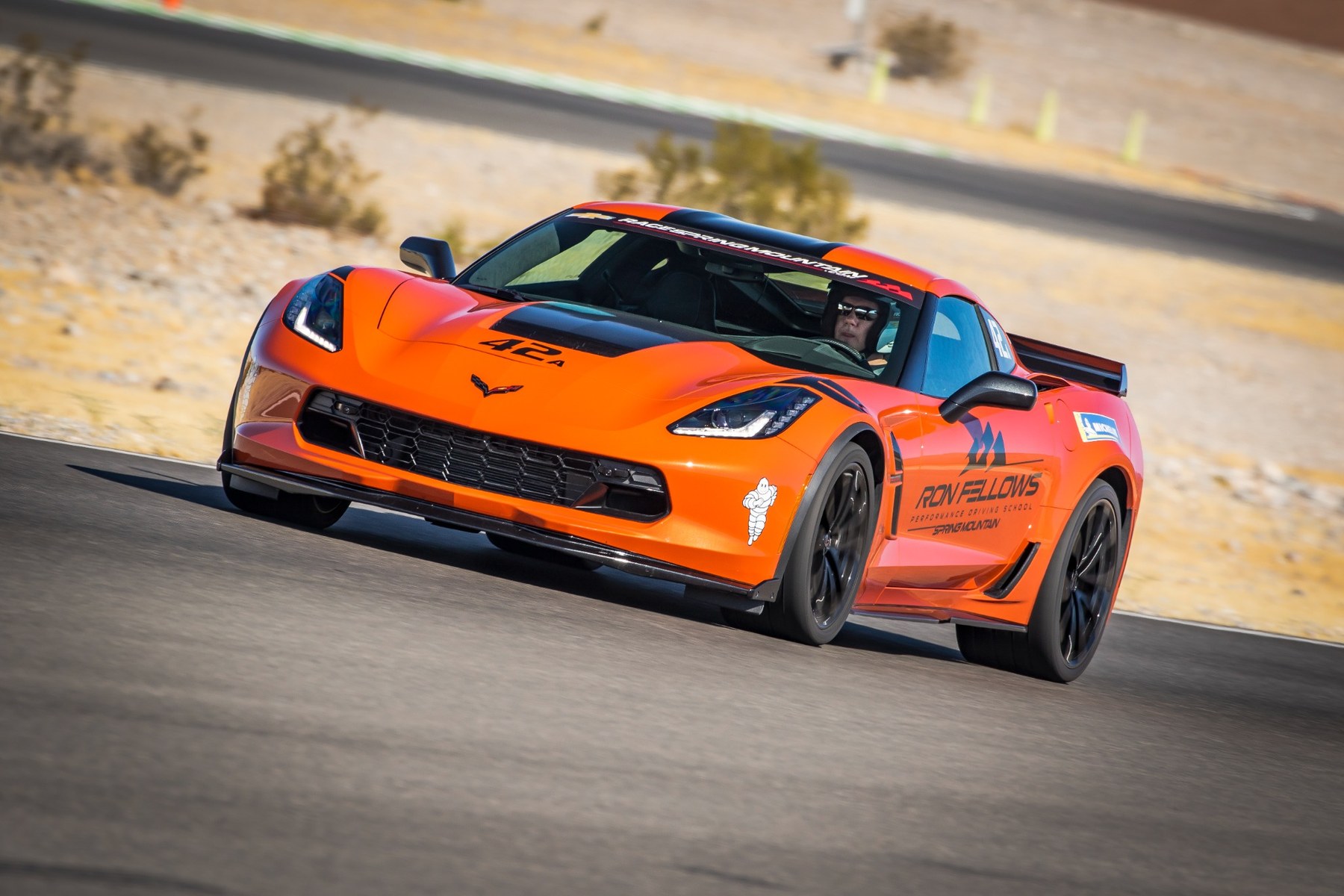 Orange Corvette cornering at Spring Mountain with desert behind it