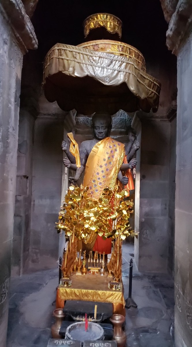A small Buddhist shrine with offerings tucked inside an Angkor temple gallery