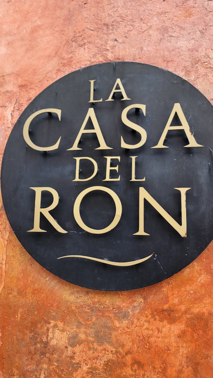 Round black and gold 'La Casa del Ron' sign on a terracotta wall in Antigua