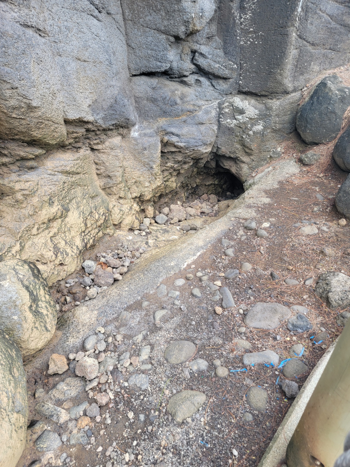 Lava rock opening of the Arahoho blowhole on Tahiti's coast, surrounded by basalt boulders