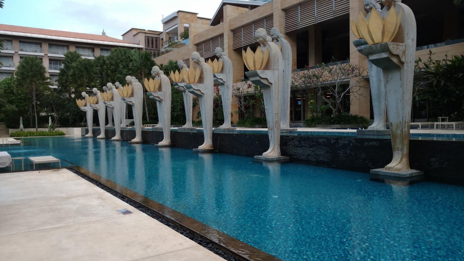 The resort pool by day, lined with unique statues holding lotus-like bowls