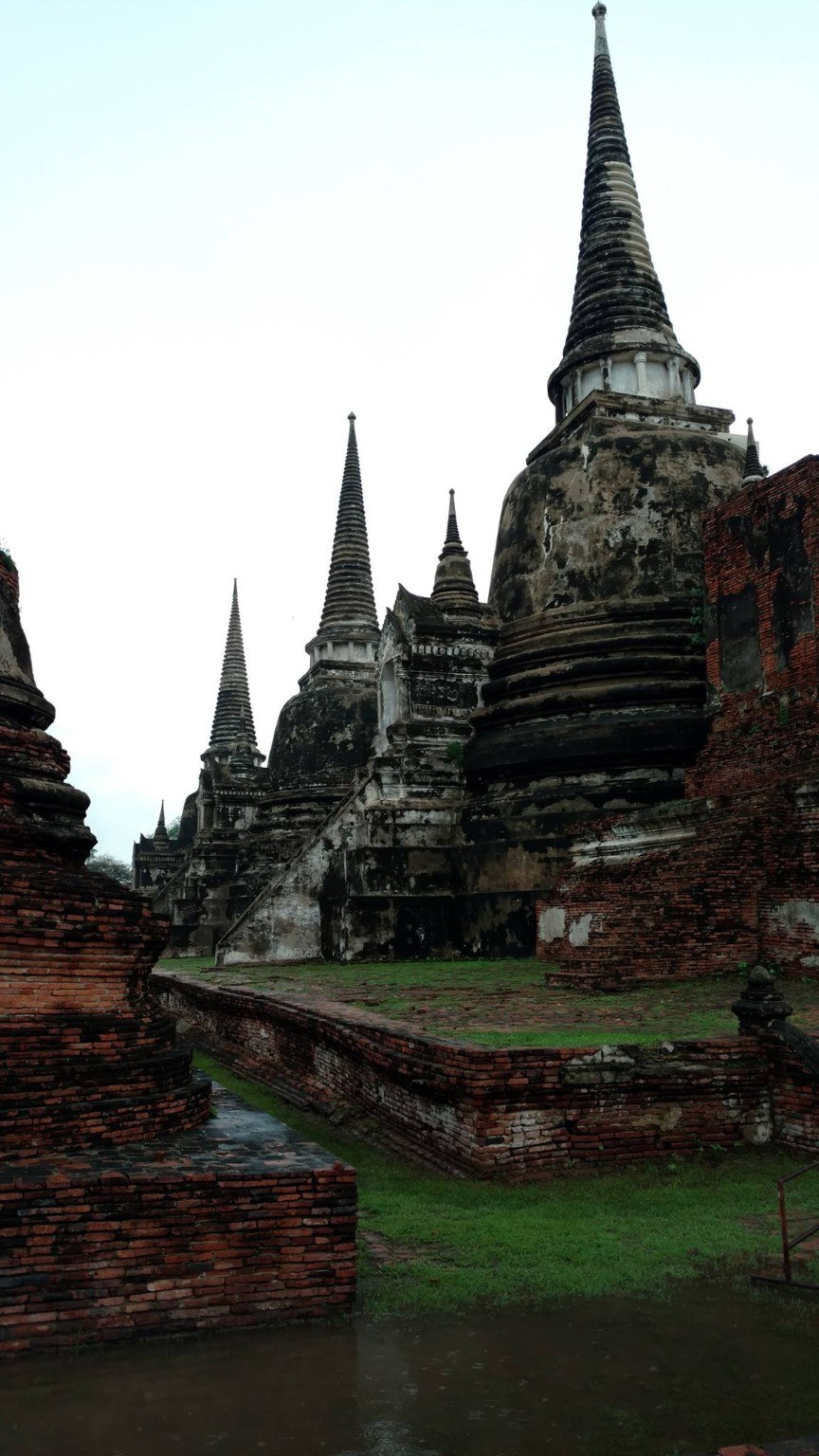 Tall chedis of Ayutthaya rising from dark brick and wet ground