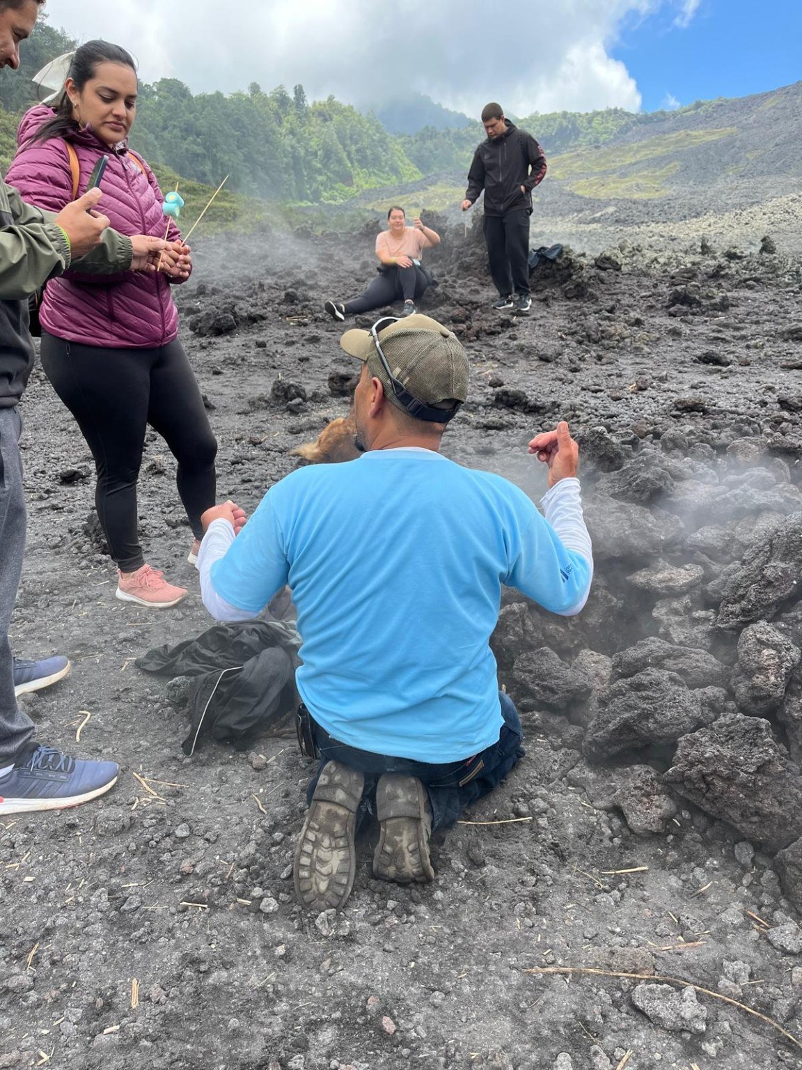 Group gathered around a Pacaya guide cooking pizza and marshmallows in a volcanic steam vent
