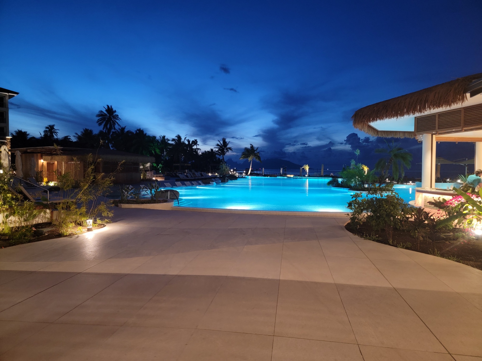 Lit resort pool at the InterContinental Tahiti at dusk with the silhouette of Moorea on the horizon