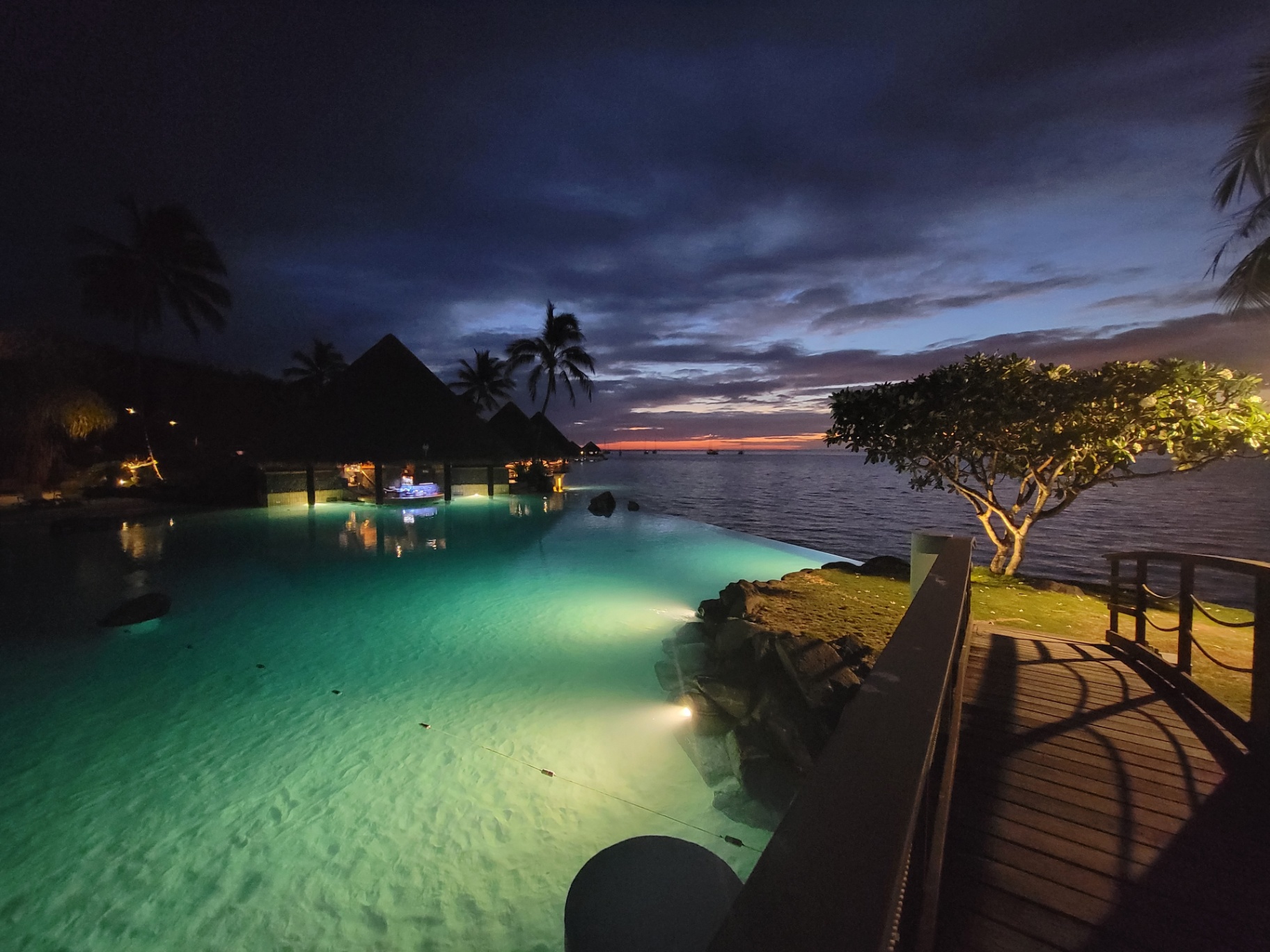 Infinity pool at the InterContinental Tahiti glowing turquoise at dusk with overwater bungalows in the distance