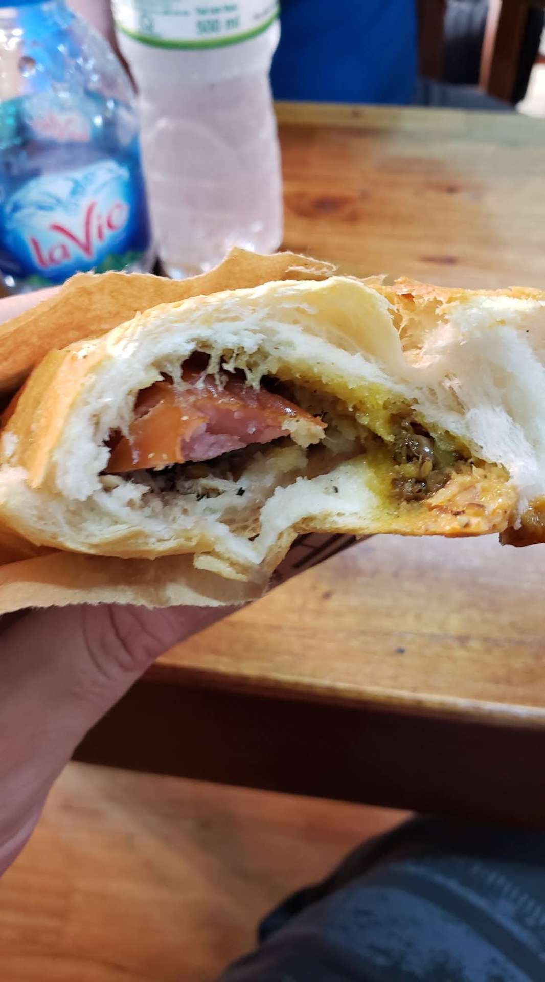 A bitten-into bánh mì sandwich from Bánh Mì Phượng in Hoi An showing tomato, pâté, and meat inside a crackling baguette