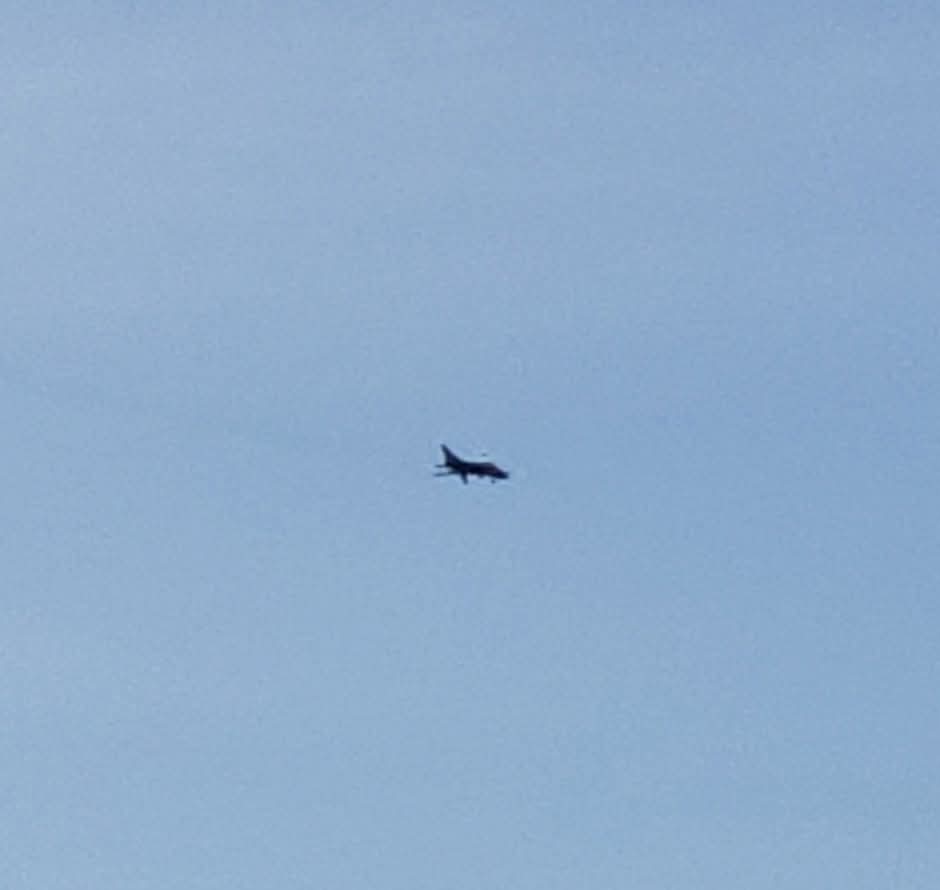 A military-style jet flying overhead against a blue sky
