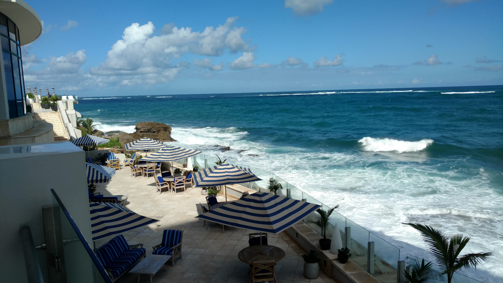 The Condado Vanderbilt's cliffside terrace with blue-and-white striped umbrellas and the Atlantic crashing below